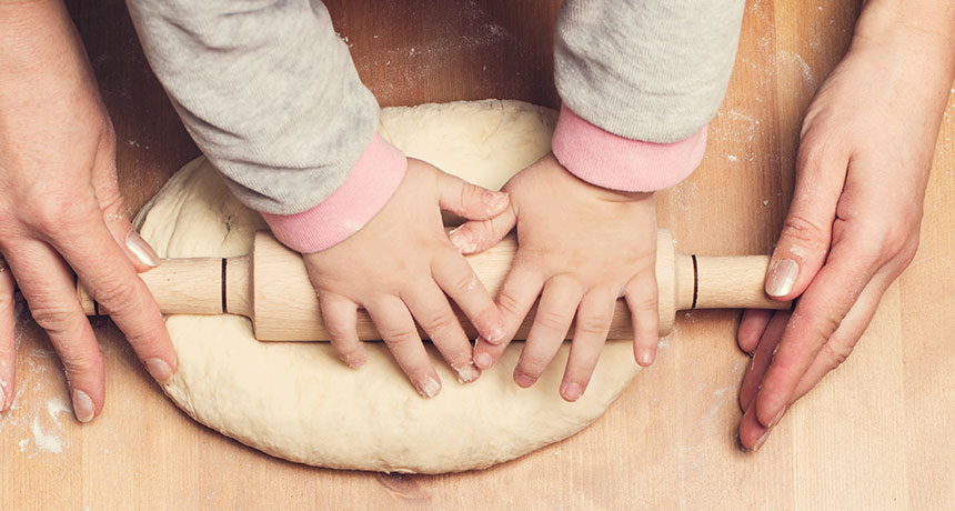 child's hands helping adult roll out dough