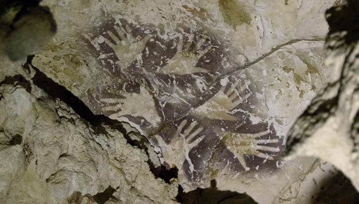 a photo showing painted outlines of human hands on a cave wall
