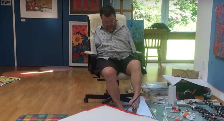 Tom Yendell sitting in a chair and painting using his feet