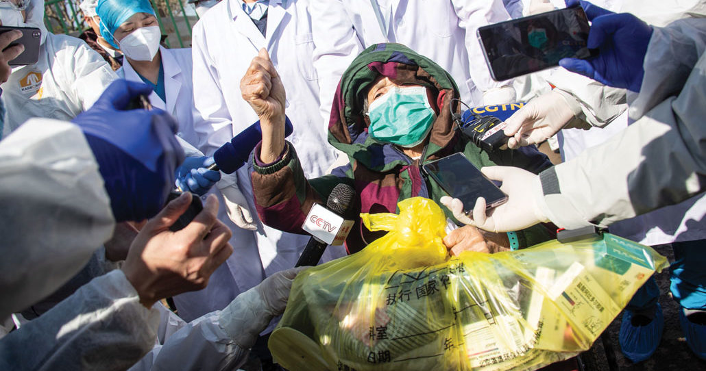 person in mask surrounded by doctors and reporters