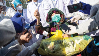 person in mask surrounded by doctors and reporters