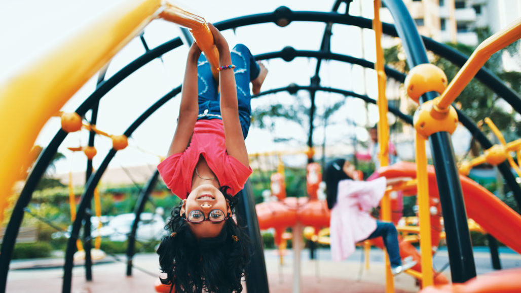 Kid hanging upside down on a jungle gym