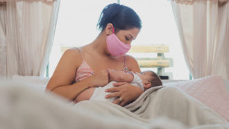Mother nursing a child wearing a mask