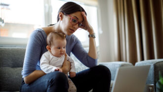 mother holding young child and looking in frustration at laptop