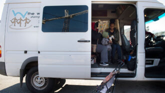 photo of a parked van with side door open; young woman and toddler sitting inside