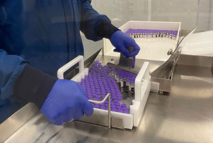 worker loading vials of COVID-19 vaccine into containers