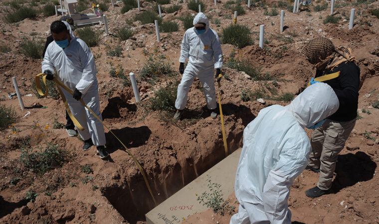 five people wearing masks surround a hole for a grave