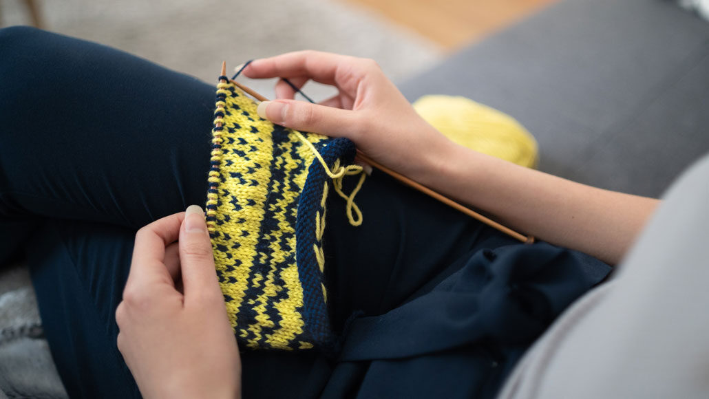 person knitting blue and yellow pattern