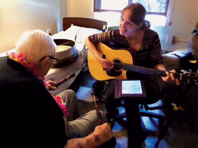 music therapist playing guitar with an old man holding drum sticks