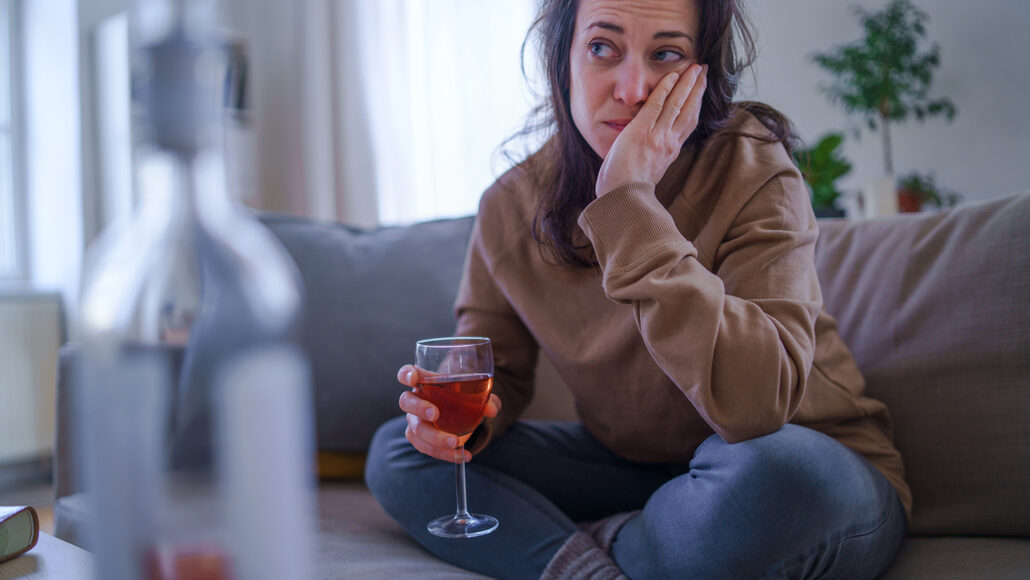 distraught woman sitting on a sofa with a glass of wine