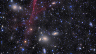 pink streaks from the Antlia supernova remnant with galaxies in the background