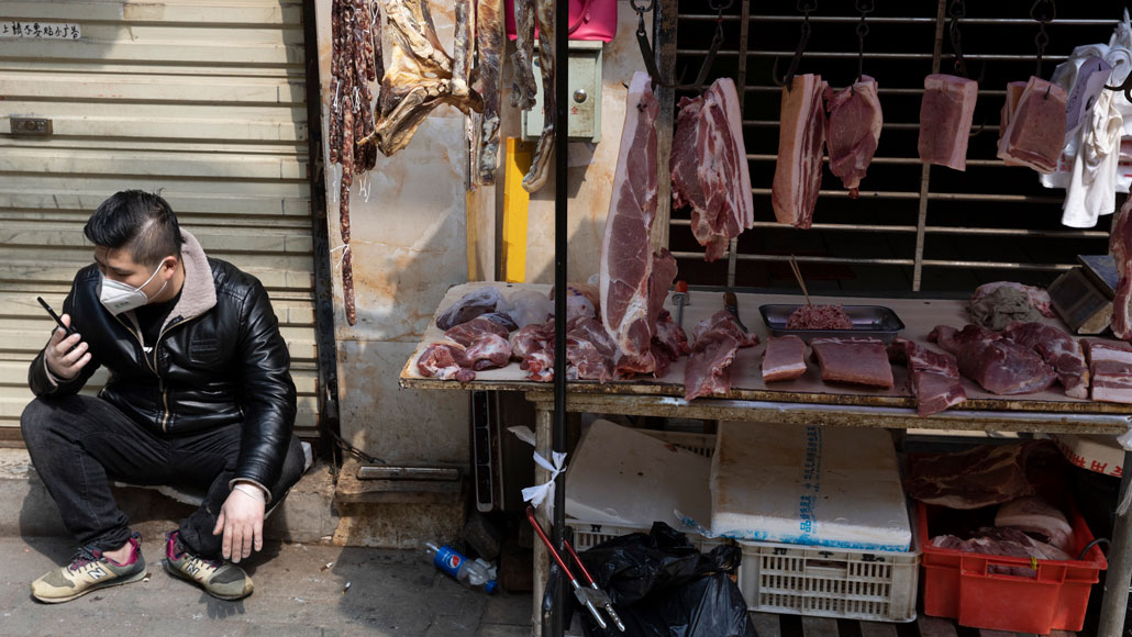 man sitting next to a meat market stand in Wuhan, China