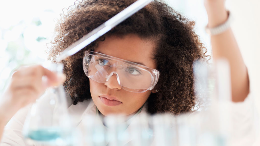 Black person wearing lab goggles and holding a scientific flask