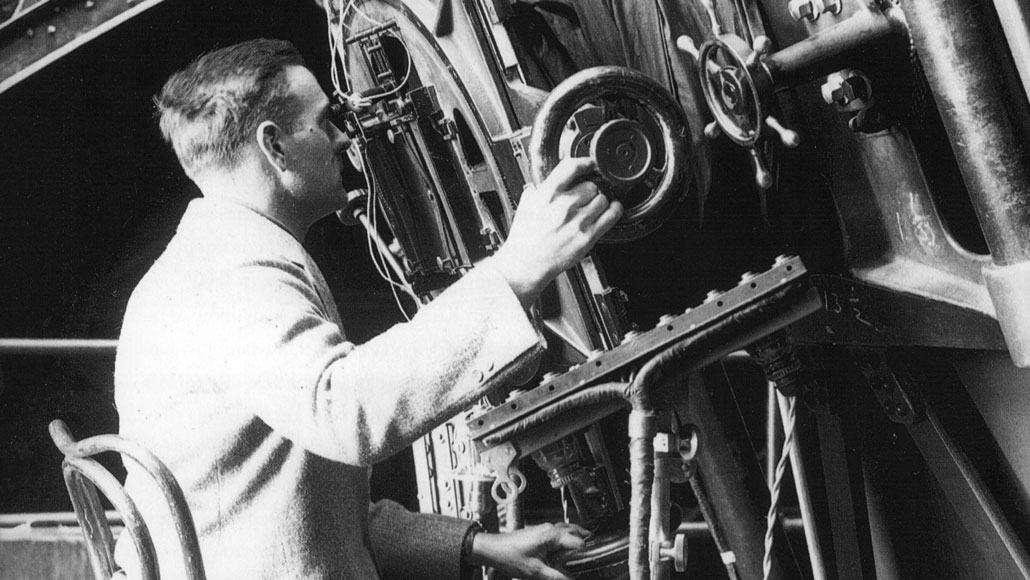 black and white photograph of Edwin Hubble looking into a telescope