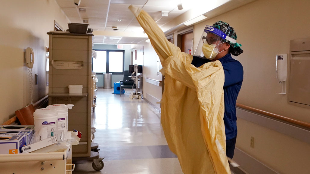 Monica Quintana wears a mask and face shield and dons a gown in a hospital hallway