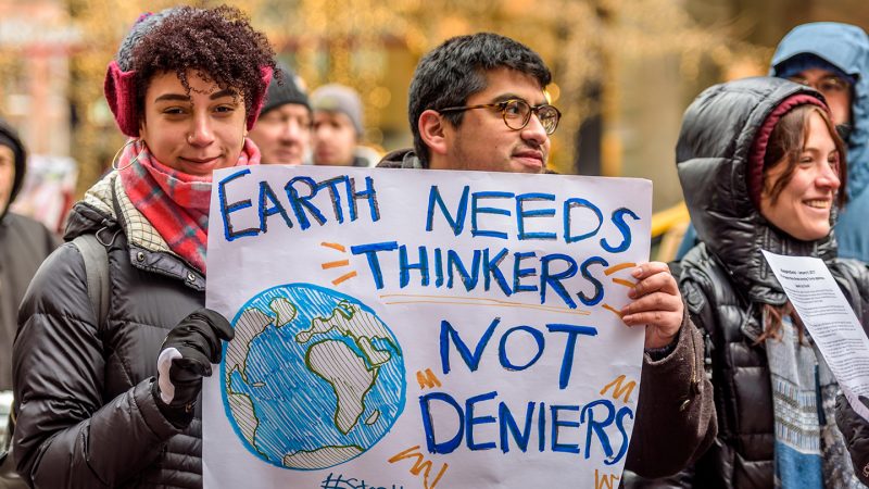 People hold up a poster that reads, "Earth needs thinkers not deniers"
