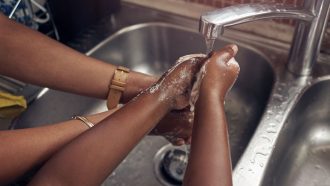 two people washing their hands under a kitchen faucet