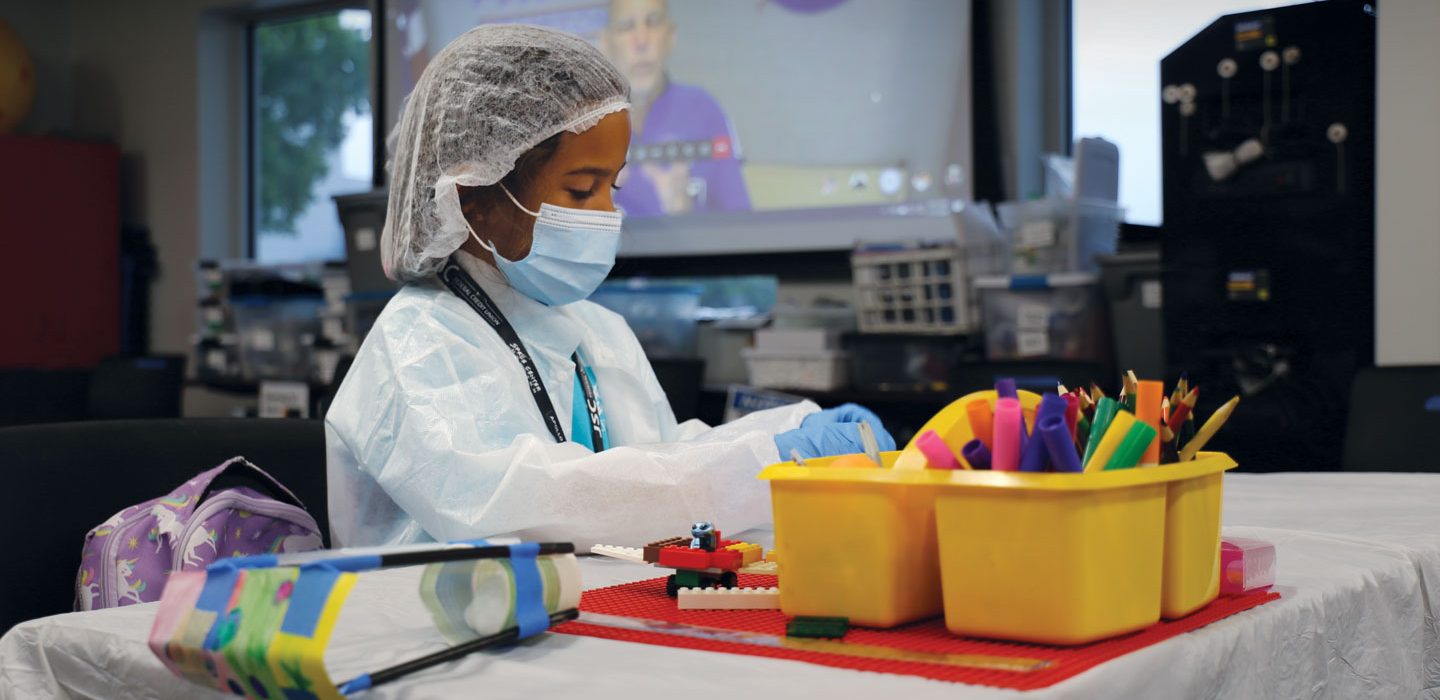 a kid in a clean room suit wearing gloves a mask and head covering playing with lego blocks
