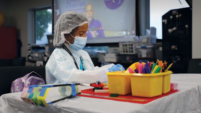 a kid in a clean room suit wearing gloves a mask and head covering playing with lego blocks