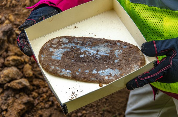hands hold a box with the "At Rest" coffin plate covered in dirt