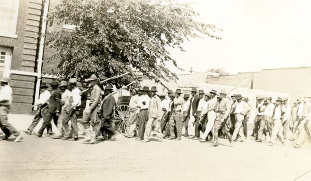 black and white image of National Guardsmen with rifles marching Black people to an internment site