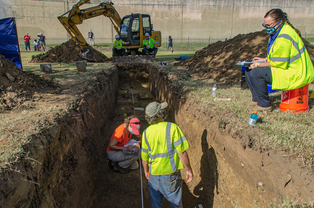 wide view down the trench of the Original 18 site with a backhoe in the background