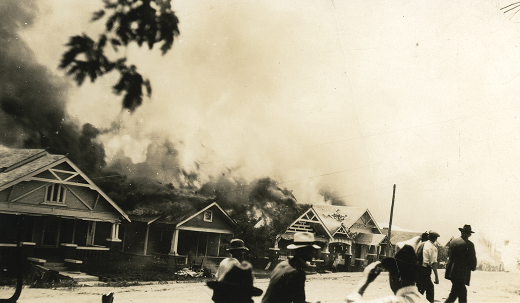 black and white image of craftsman homes on fire with white vigilantes in the foreground