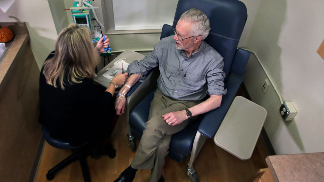 man sitting in a chair receives an infusion of aducanumab