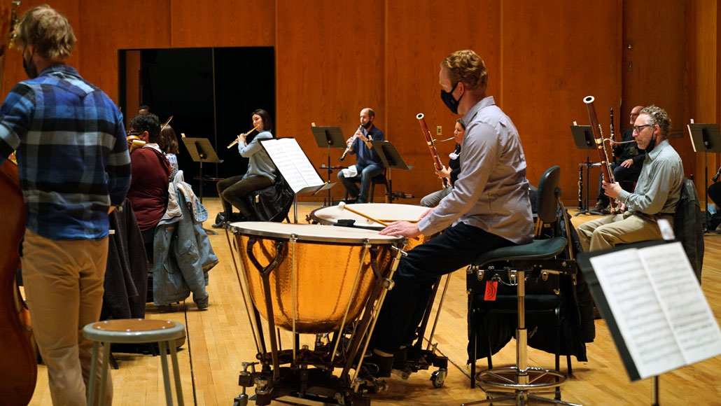 Michael Pape sits behind two timpani drums while others rehearse in the background