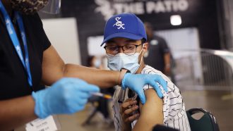 a young man in a White Sox hat receives a COVID vaccine in his left arm