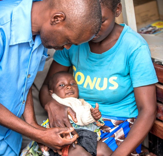 man vaccinates a baby laying in a mother's lap