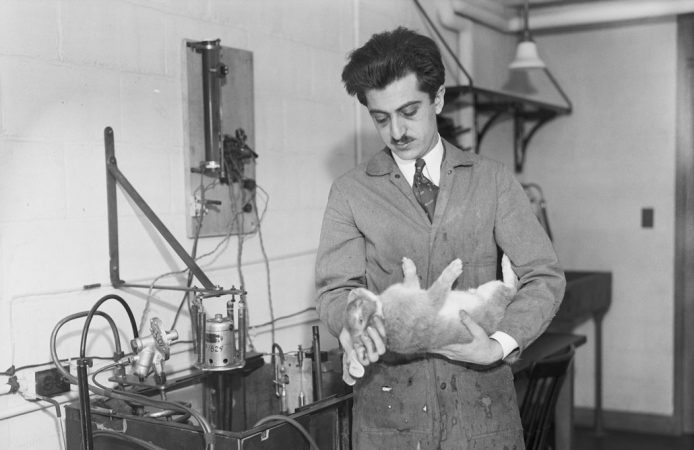 black and white photo of a man with a moustache in a lab coat holding a rabbit