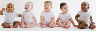 five babies of different ethnicities sitting, all wearing white onesies