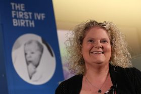 photograph of a blond woman in front of a poster of her baby picture