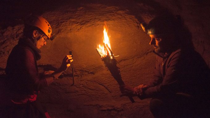 two researchers, one holding a torch in a dark cave