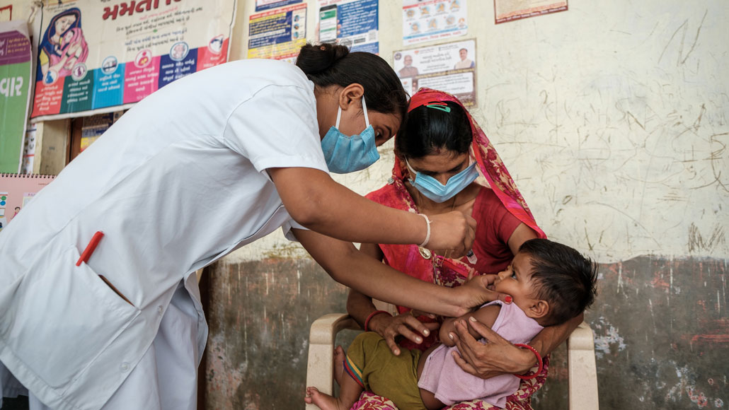a small child, being held by her mother, is given a vaccine by a nurse in India