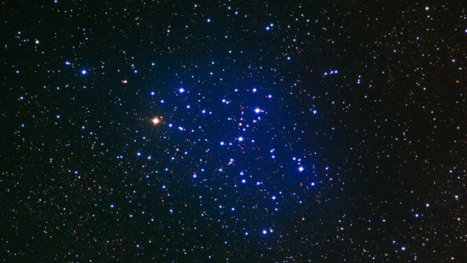 telescope image of a star cluster, which is surrounded by a blue haze