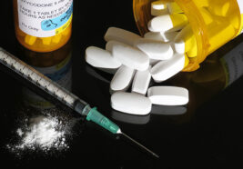 a syringe, oxycodone pills, and a crushed pill on a black background