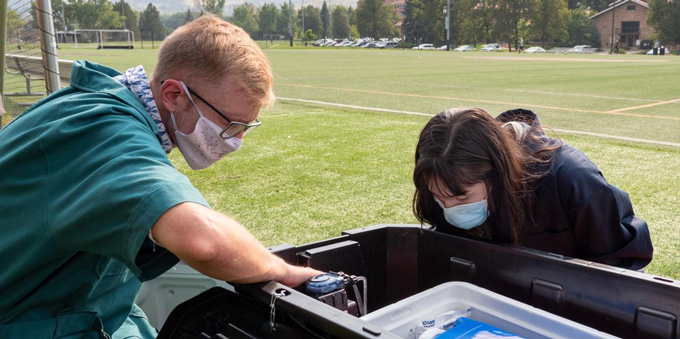 two people check a wastewater monitoring station on a field at the University of Colorado Boulder campus