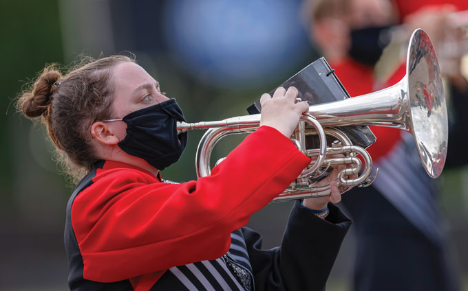 a marching band member wears a mask while playing the flugelhorn