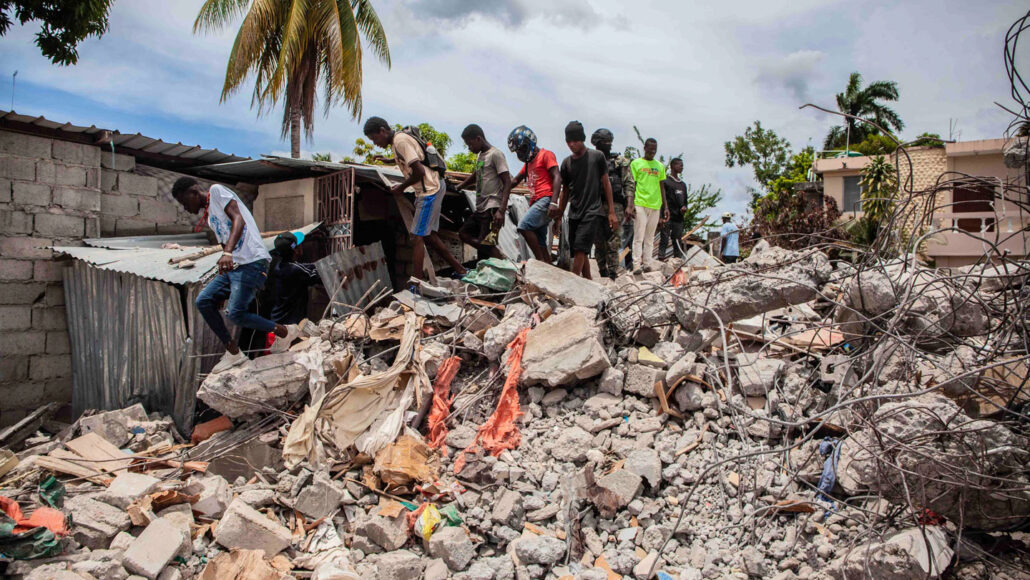 people climb over building rubble in Les Cayes