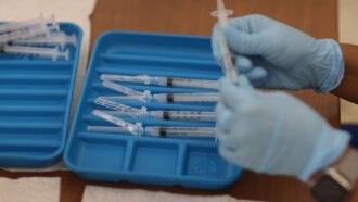 Moderna COVID-19 vaccines being prepared in syringes, held by a person wearing blue gloves