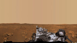 A photo of the Martian landscape with part of the Perseverance rover in the foreground