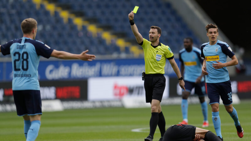 a referee holds up a yellow card amid during a soccer game in Germany