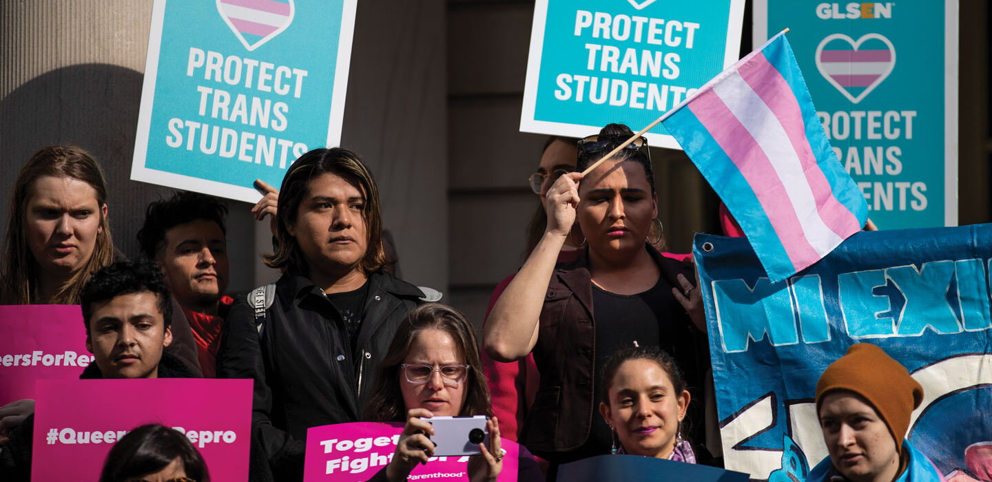 people hold posters and flags in support of transgender people