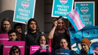 people hold posters and flags in support of transgender people