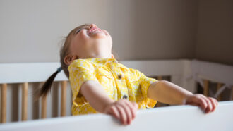 Baby wearing yellow, laughing with head tilted upwards