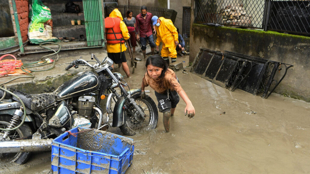 persoon die door de overstroomde Bishnumati-rivier waadt, leunend op een motorfiets