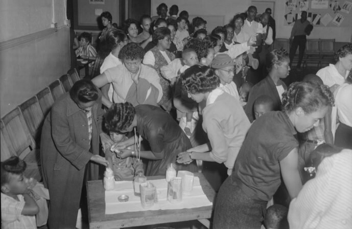 black and white photo of children and adults, all of whom are black, at a vaccine clinic