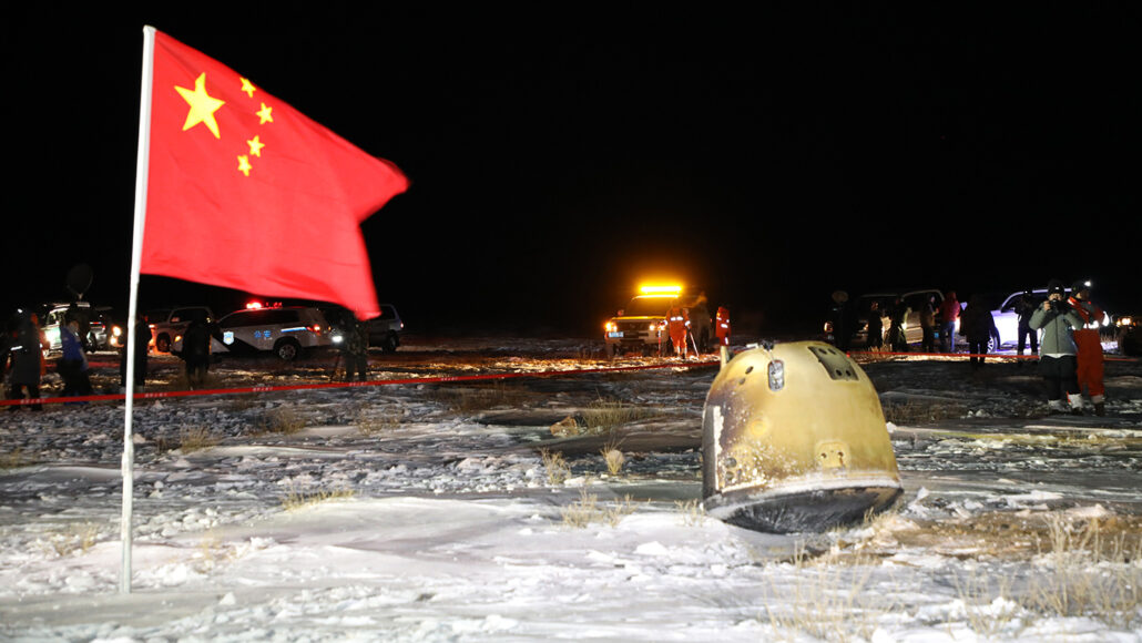 Een capsule met maanstenen naast een Chinese vlag met voertuigen op de achtergrond